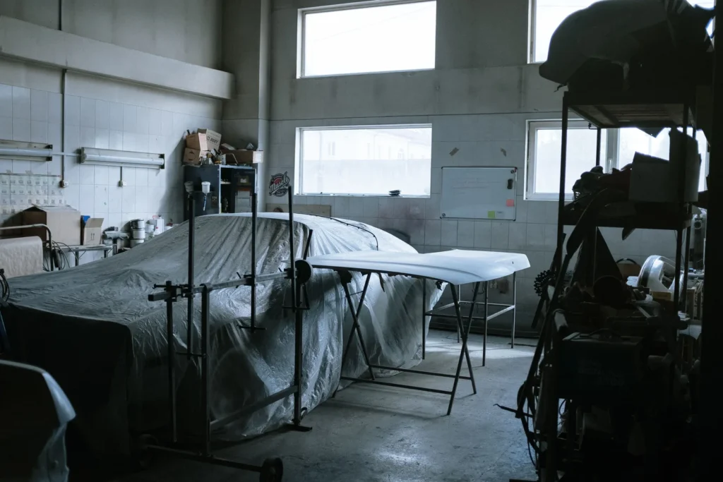 A covered car sitting inside an auto repair shop surrounded by tools and equipment