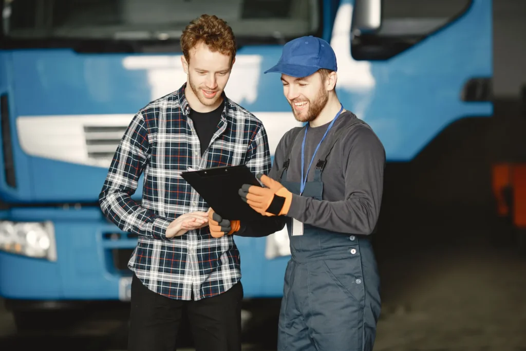 A vehicle owner and a mechanic in uniform discussing a repair inside a garage