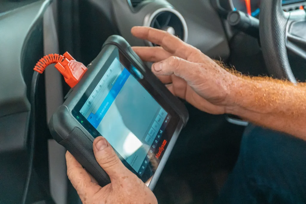 A technician holding a diagnostic tablet in the driver seat of a vehicle