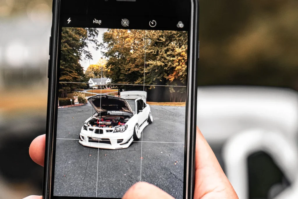 A person photographing a car with a smartphone, the vehicle visible on the screen