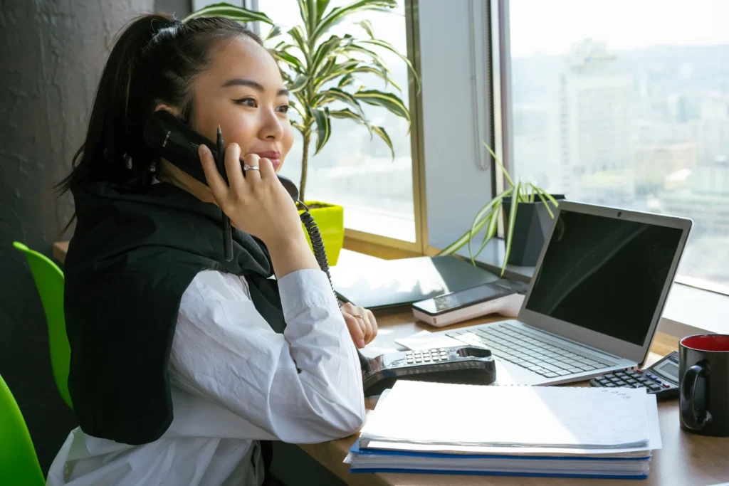 A person on a phone call at a desk with a laptop and paperwork