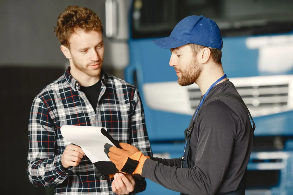 A mechanic in uniform explaining vehicle maintenance to a customer inside a garage