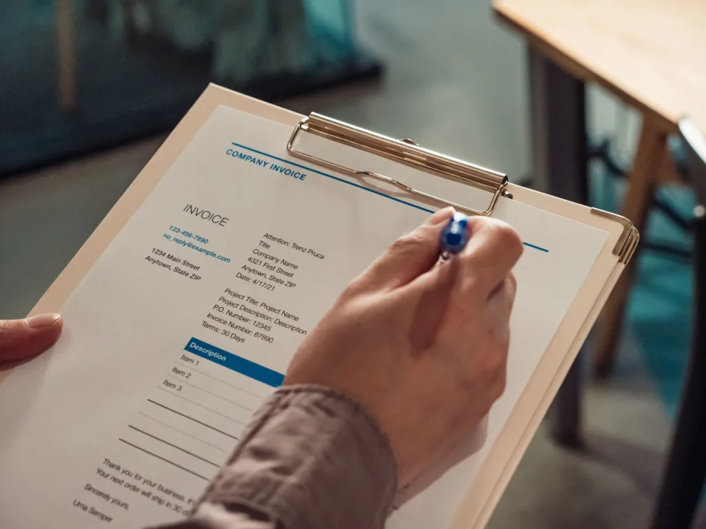 A hand holding a pen over an itemised service invoice on a clipboard