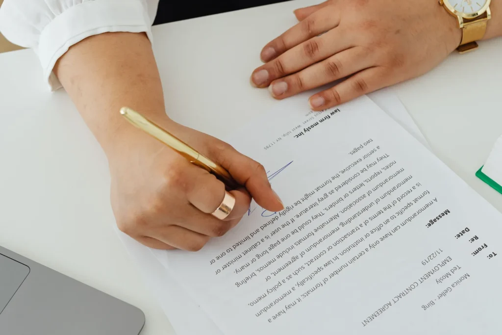 Hands signing a printed document at a desk in an office