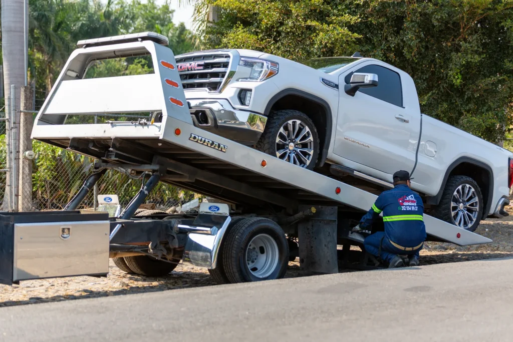 A tow truck operator loading a white pickup truck onto a flatbed on a city street