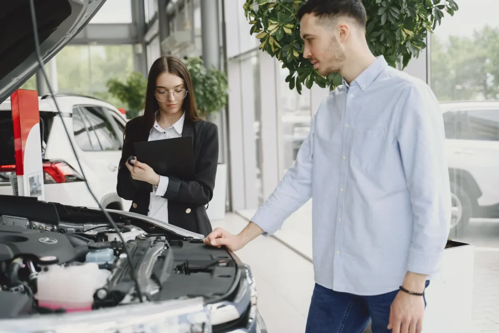 Two people examining the engine of a white car with the hood raised