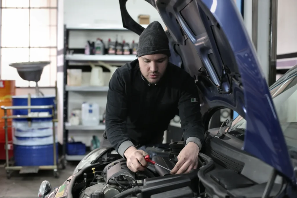Mechanic working under the raised hood of a car in a workshop