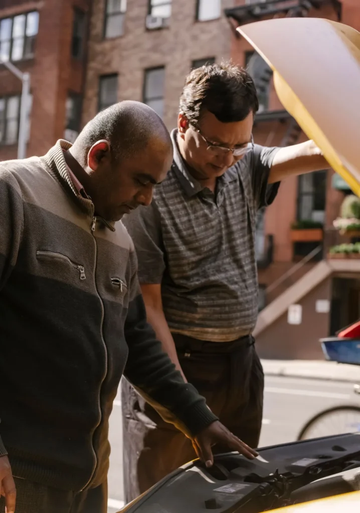Two men examining the engine bay of a car with the hood raised at the roadside