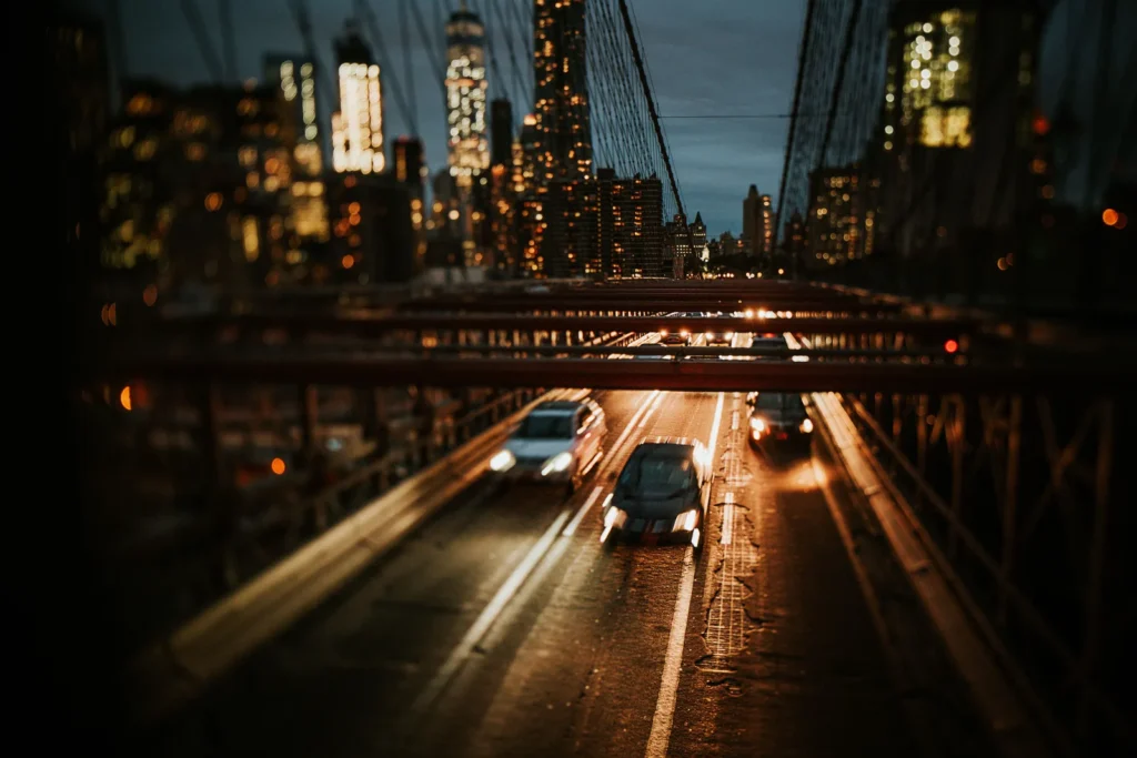 Cars crossing the Brooklyn Bridge at night with the Manhattan skyline behind