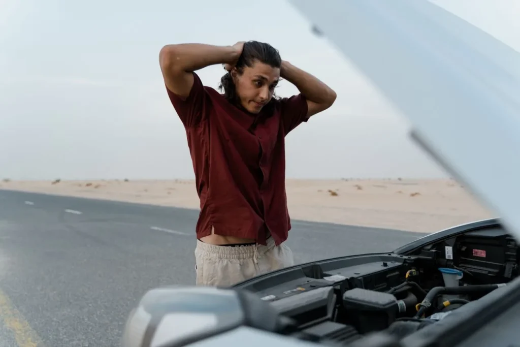 Driver stranded beside a car with the hood raised on a desert road
